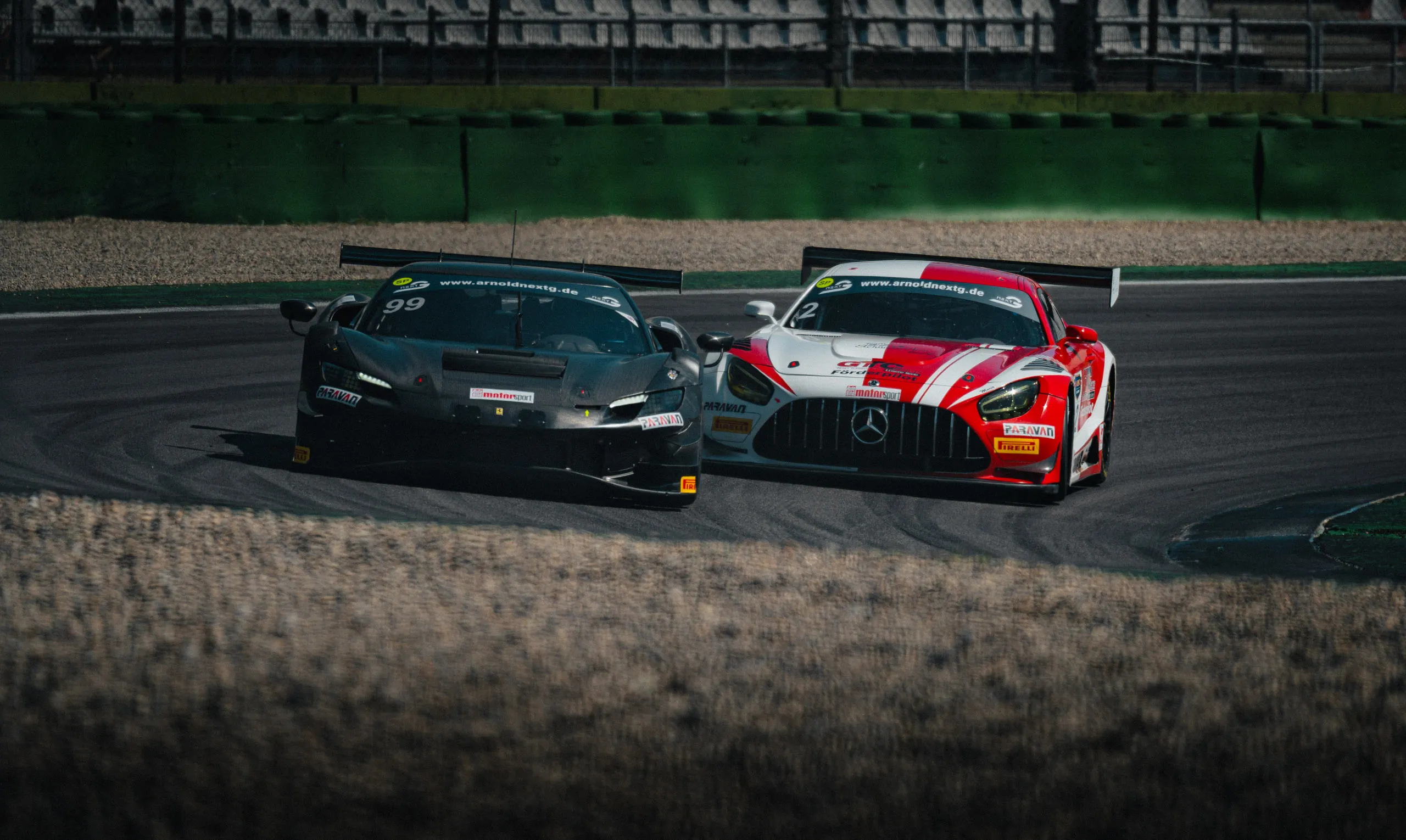 A black Ferrari 296 GT3 with start number 99 and the red-and-white Mercedes-AMG GT3 from Schnitzelalm Racing are racing side by side through a turn at the Hockenheimring.