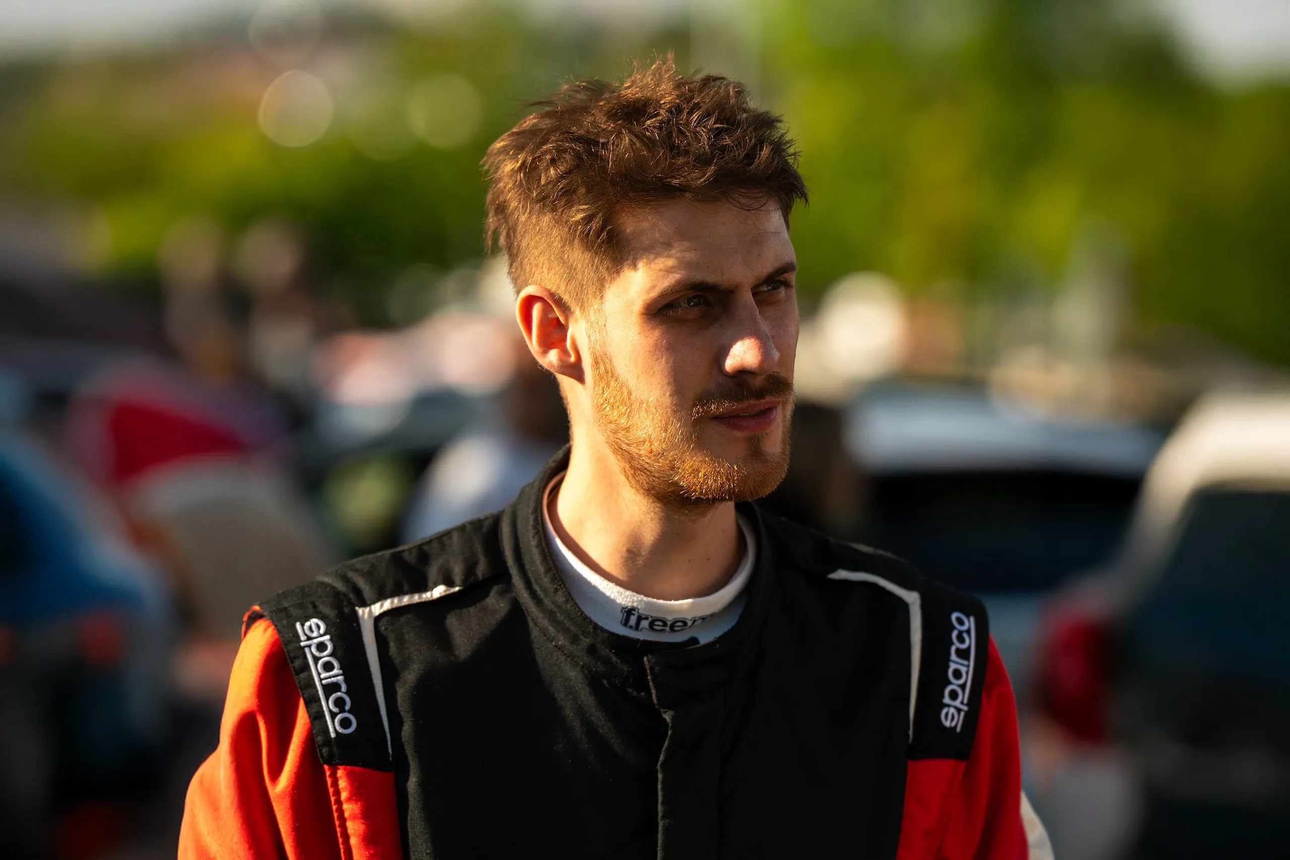 Porträt von Rallyefahrer Florian Schwenker im schwarz-roten Rennoverall, aufgenommen im Abendlicht des Servicebereichs.