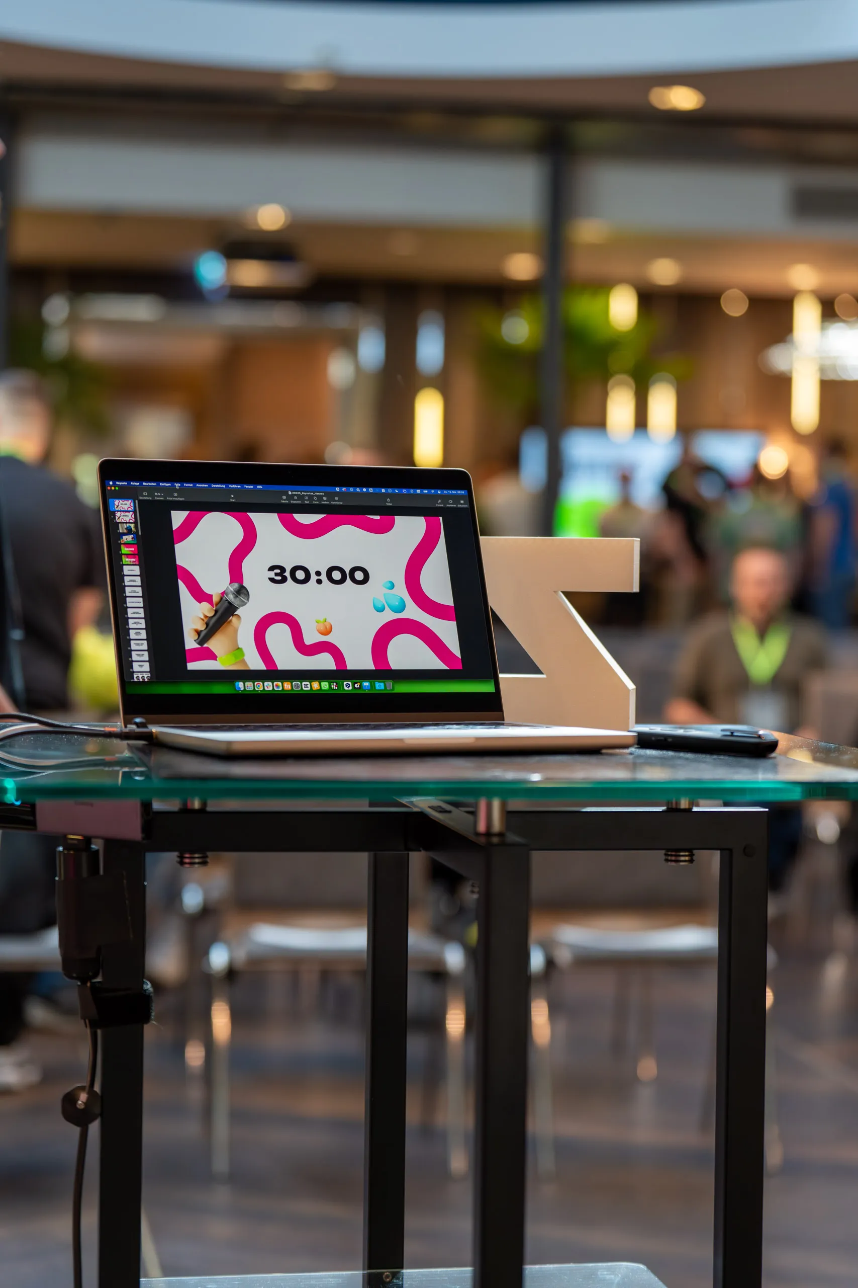 Laptop mit laufendem Präsentationstimer bei 30:00 auf einem Glastisch, daneben ein großer Buchstabe „Z". Aufgenommen vor Beginn des Hannes Zwetschke Community-Day 2025.