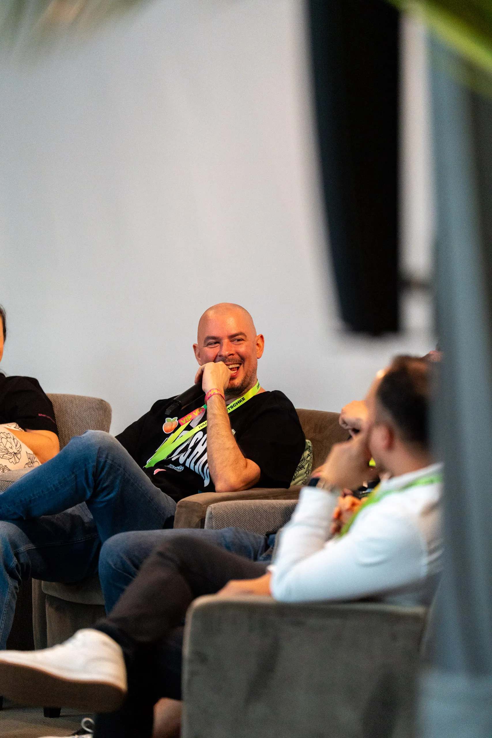 Hannes Zwetschke lacht während einer Panel-Diskussion beim Community-Day 2025, entspannt im Sessel zurückgelehnt, das Mikrofon in der Hand.
