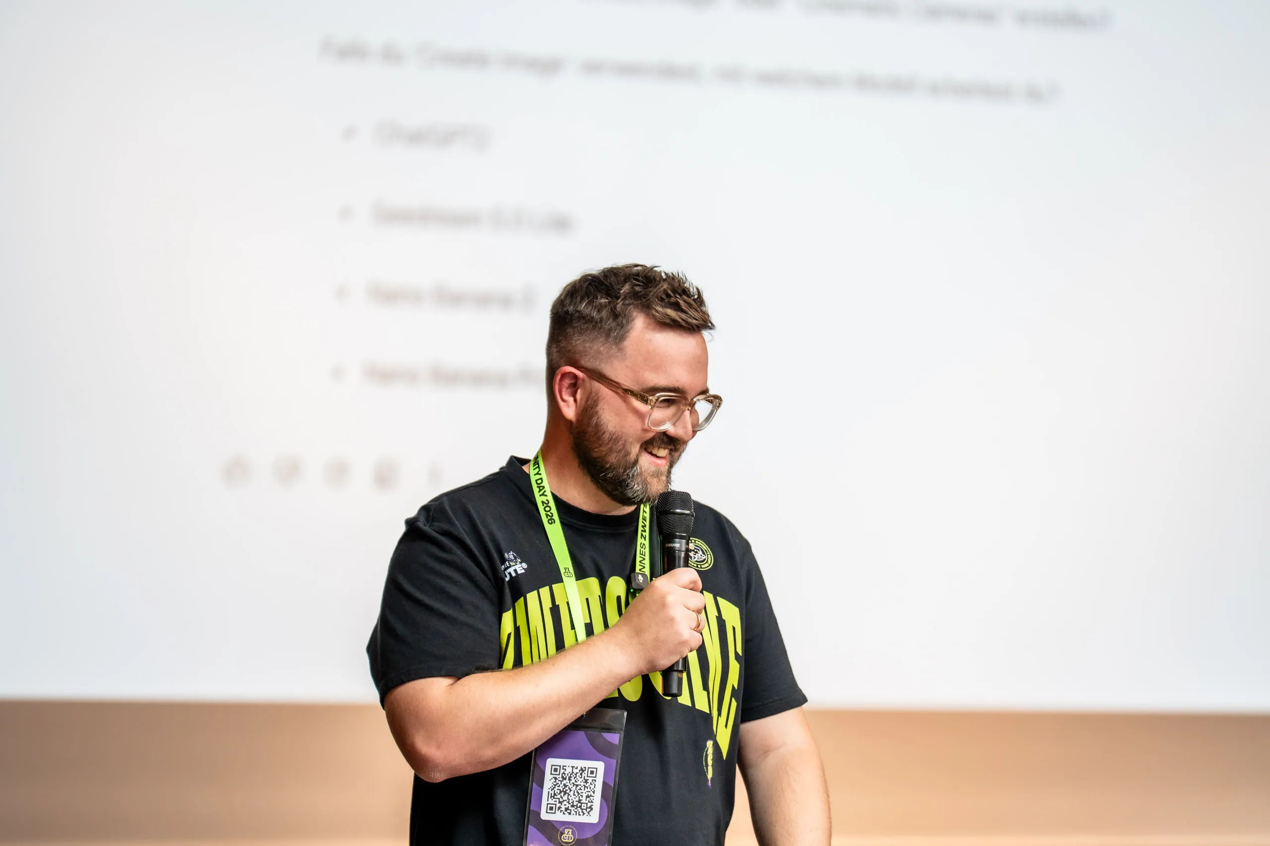 Florian Geißler, Art-Director und Prokurist bei zwetschke, spricht mit Mikrofon über KI-Workflows beim Zwetschke Community Day 2026, im Hintergrund eine Folie mit einer Liste von KI-Bildtools.