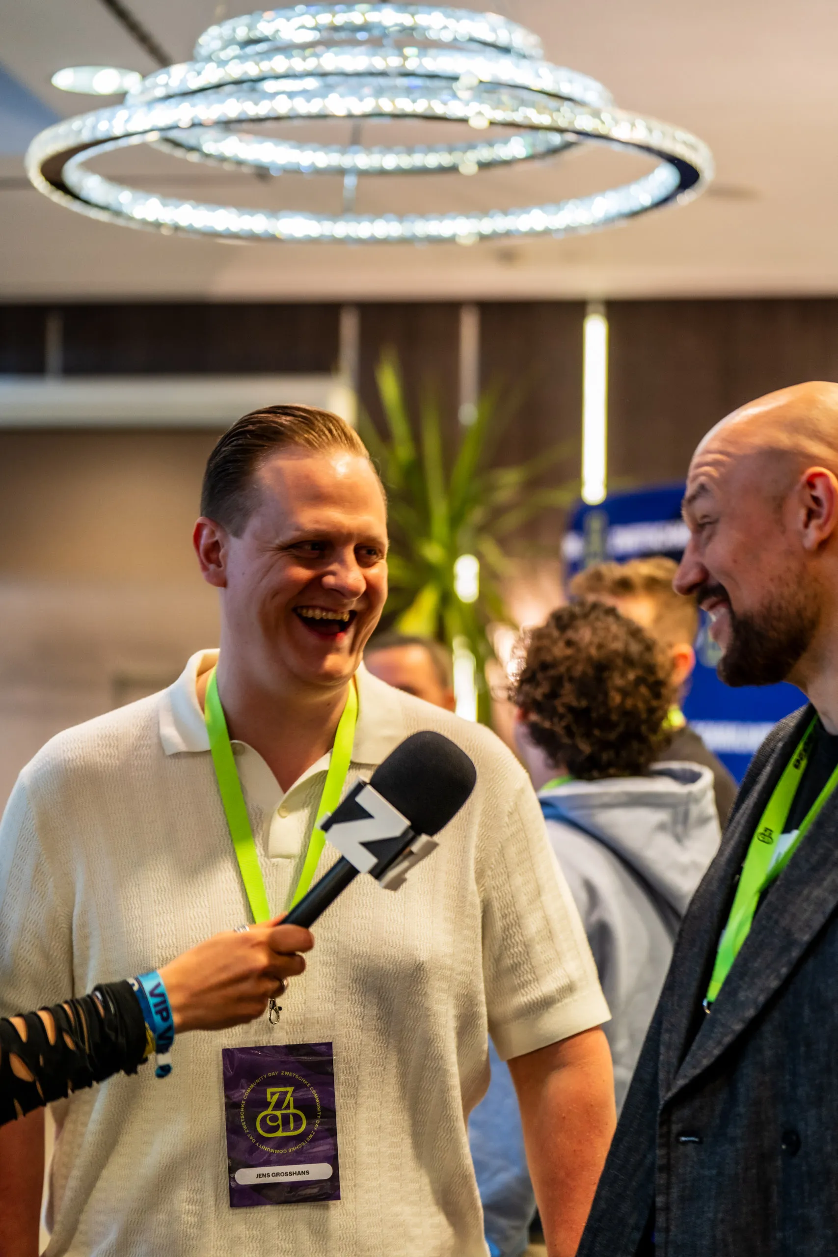 Jens Grosshans lacht mit einem Z-Mikrofon in der Hand während eines Interviews beim Zwetschke Community Day 2026, unter einem großen Ringleuchter.