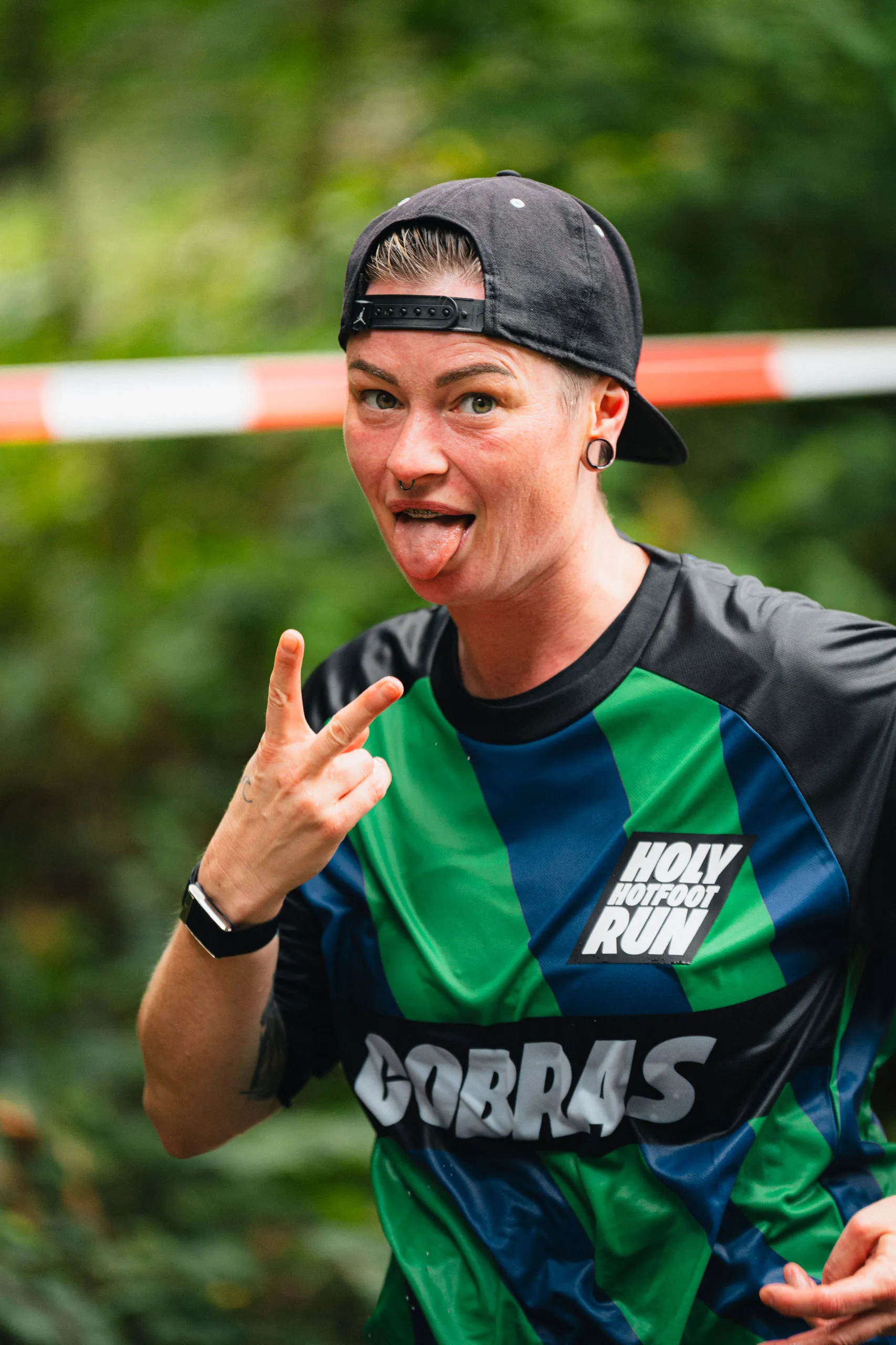 A runner in a green-and-blue "Cobras" jersey sticks out her tongue and throws a rock sign at the camera.