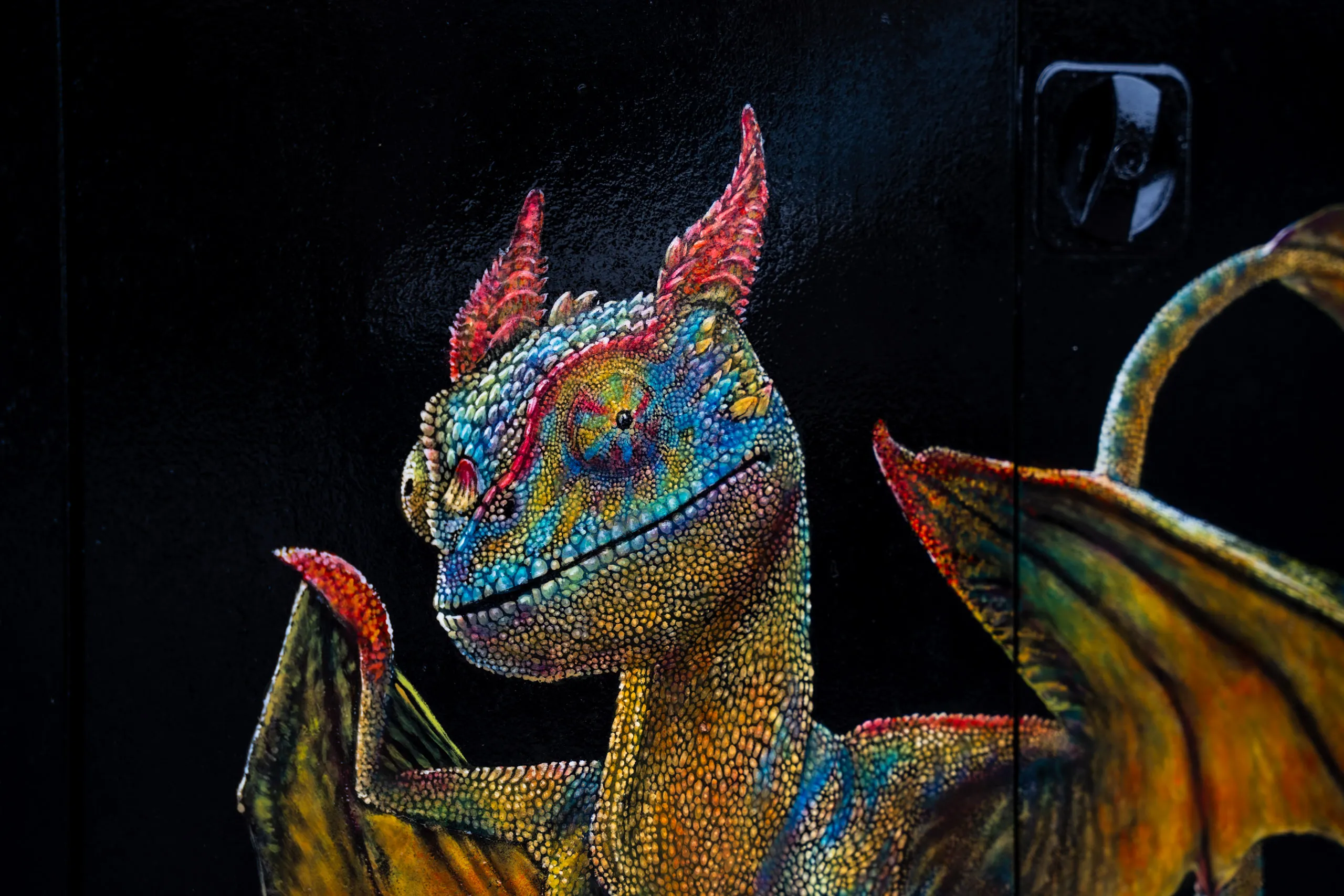 Close-up of the dragon artwork on the cabinet: head and wings in blues, greens and yellows with finely stippled scales and red horns against a black background.