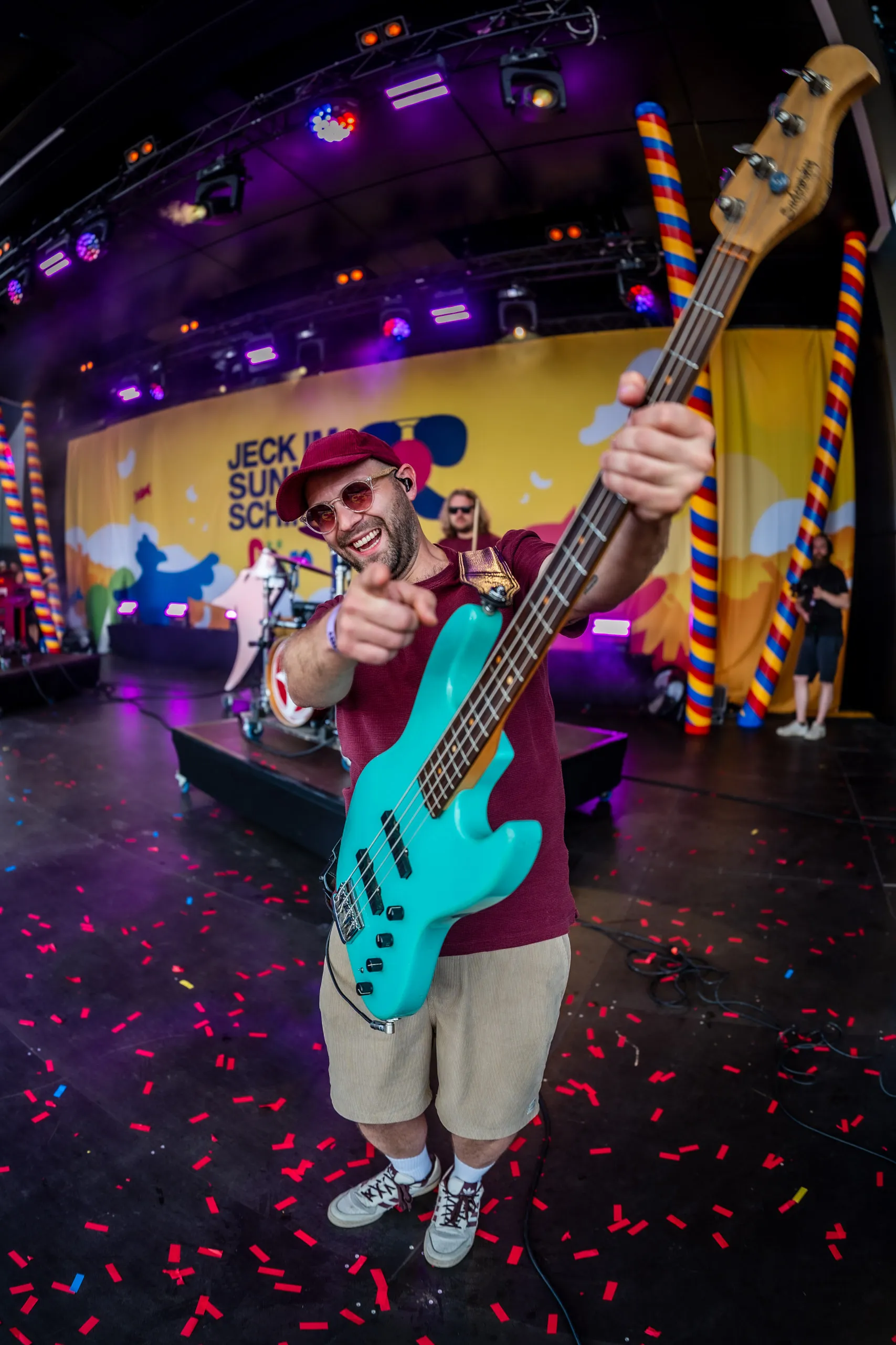 Alexander Lemke, bass player of the band Lupo, pointing at the camera with his turquoise bass, red confetti scattered across the stage floor.