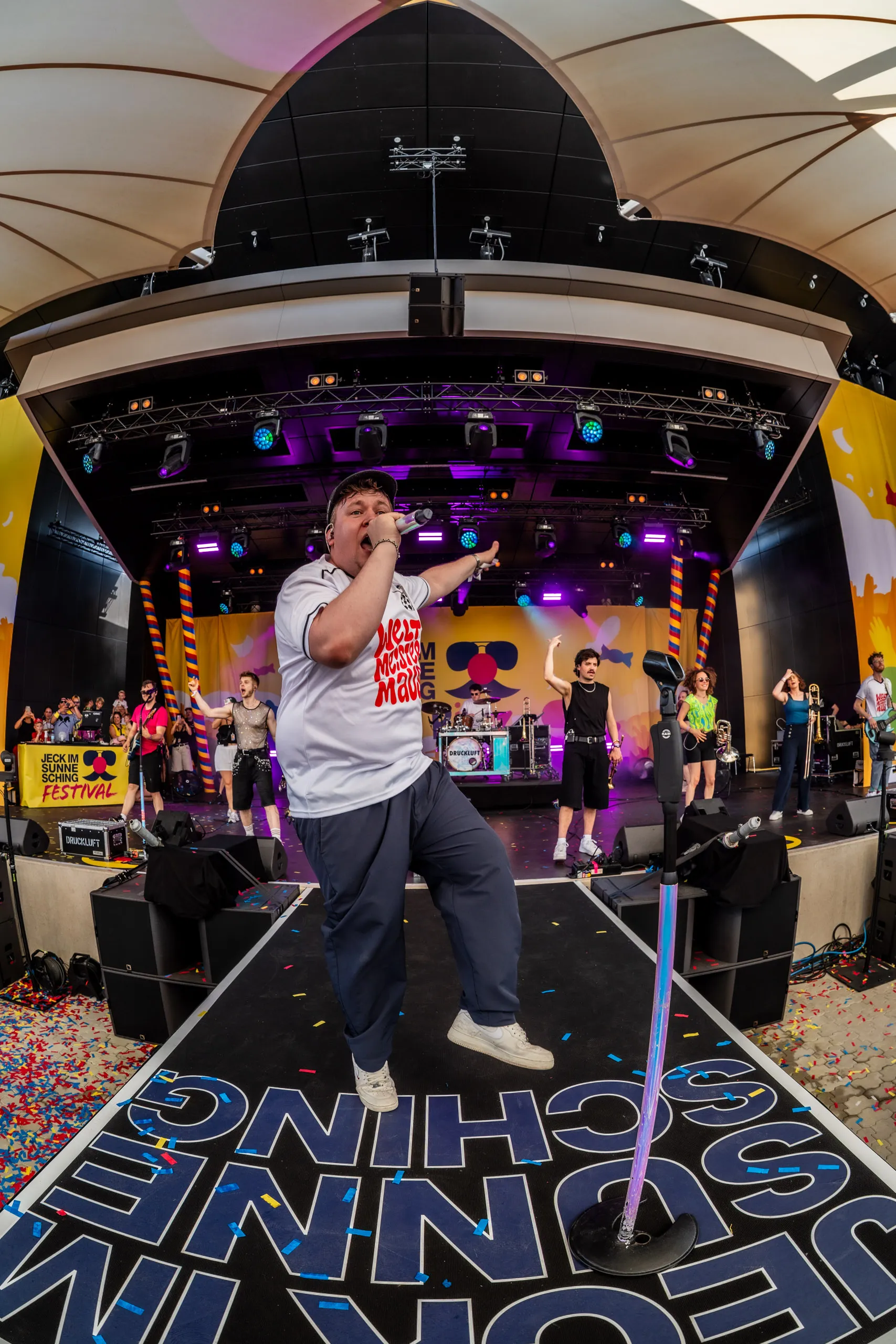 Florian Hertel, singer of Druckluft, on the stage catwalk at Jeck im Sunnesching, the full band behind him.