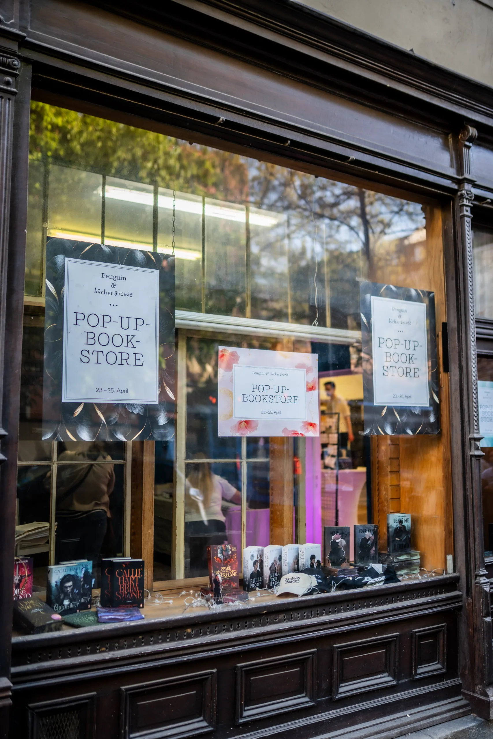 Shop window of the pop-up book store with Penguin & Bücherbüchse posters, romance titles lined up in front and a cap reading "Fantasy Reader".