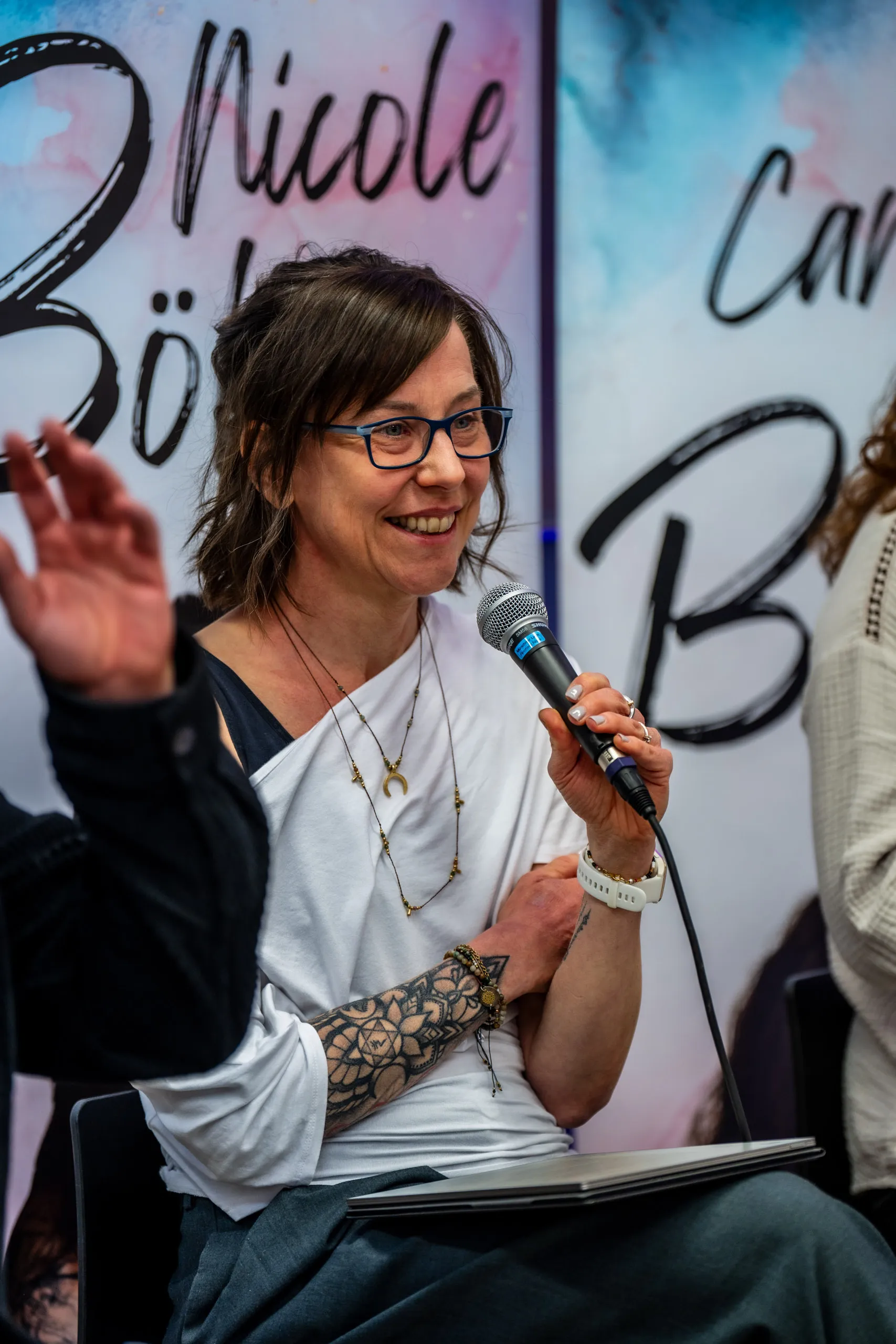 Nicole Böhm with a microphone during the talk at the pop-up book store, the authors’ name banners behind her.