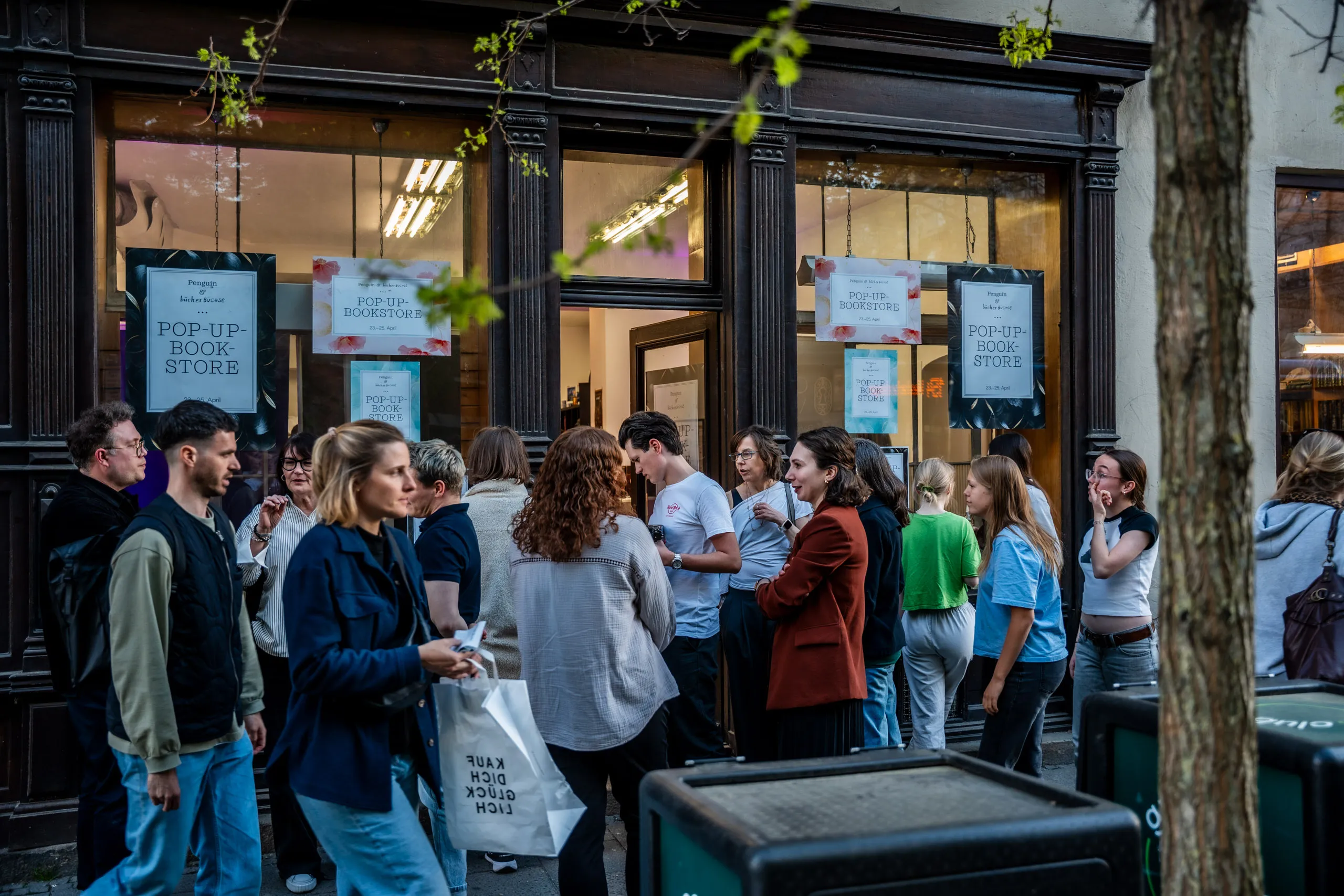 Visitors gathered outside the pop-up book store in Munich’s Maxvorstadt in the evening, Penguin & Bücherbüchse posters in the windows.