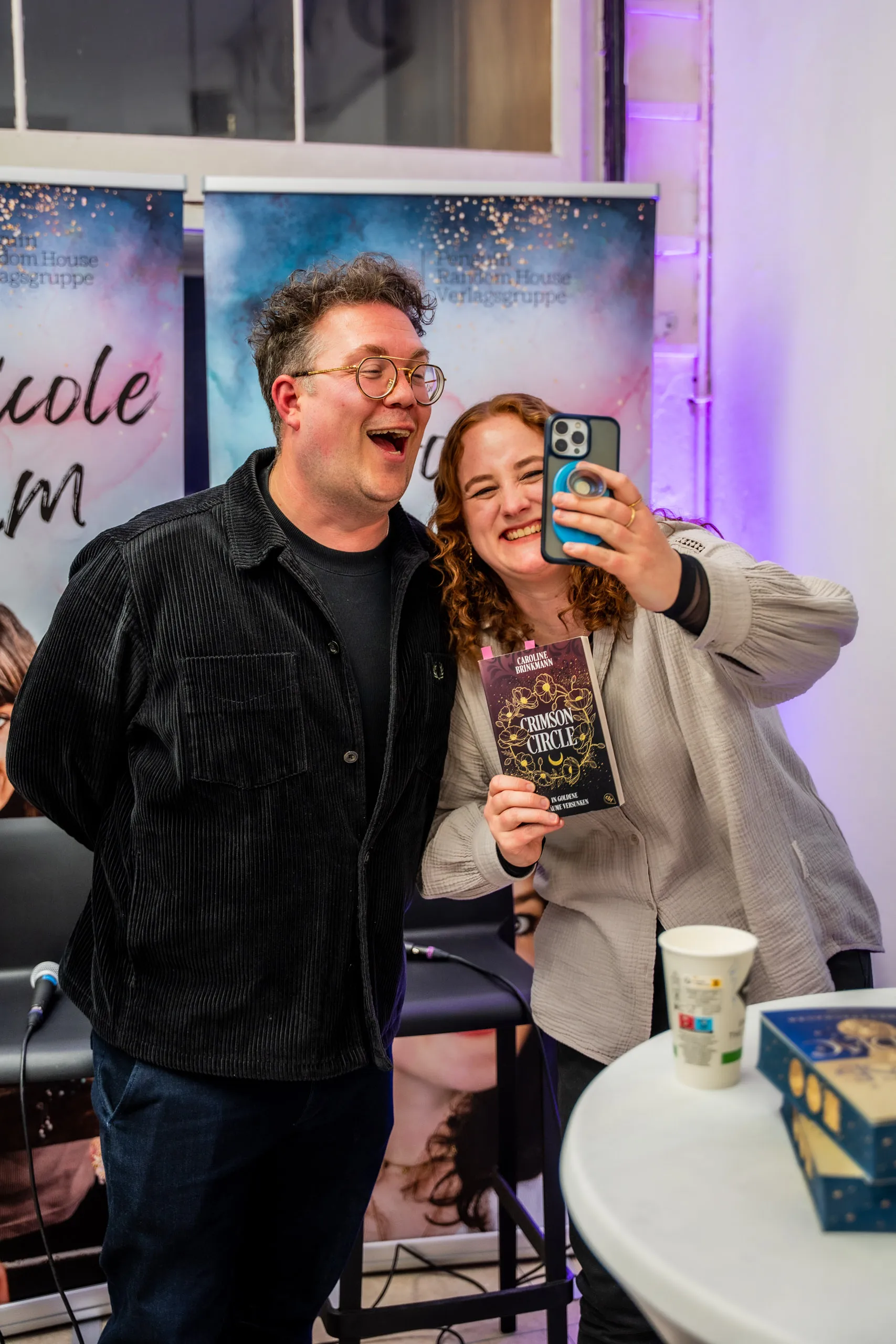 Caroline Brinkmann taking a selfie with Thomas Sachsenmaier, holding her novel "Crimson Circle".