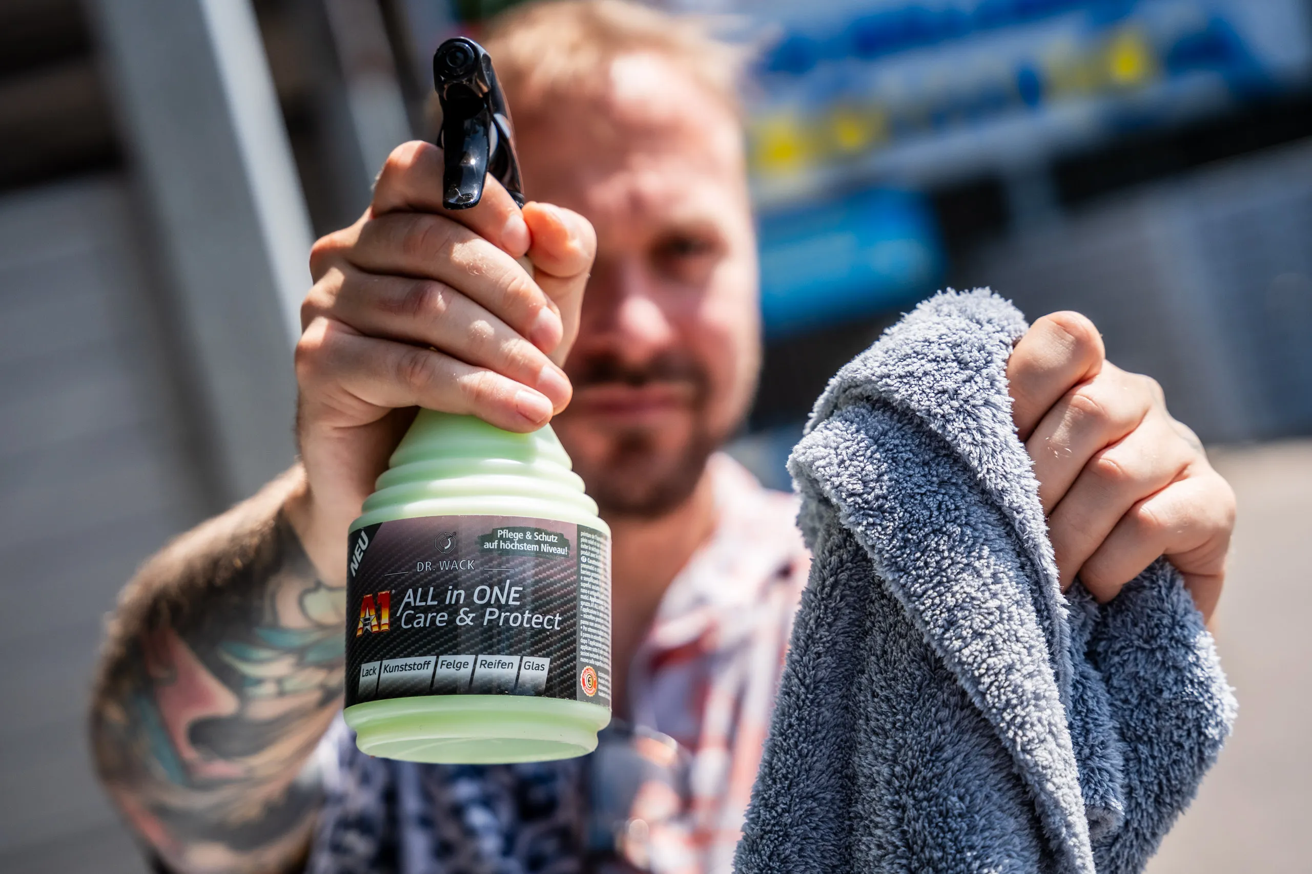 Raphael Siegmund holding out a spray bottle of A1 All in One Care & Protect by Dr. Wack towards the camera, a microfibre cloth in his other hand.
