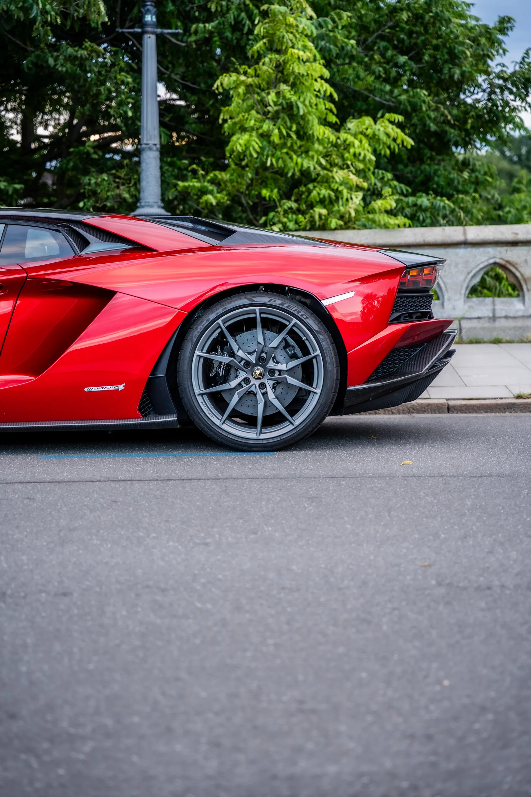 Rear section of a red Lamborghini Aventador S parked at the kerb, close-up of wheel, brake and diffuser.