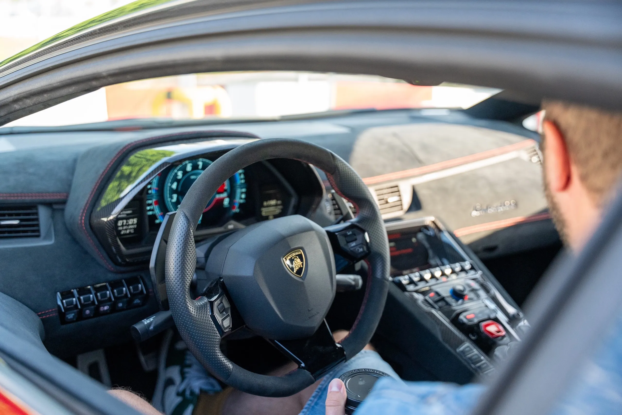 View across the steering wheel of a Lamborghini Aventador onto the digital cockpit, Raphael Siegmund at the wheel.