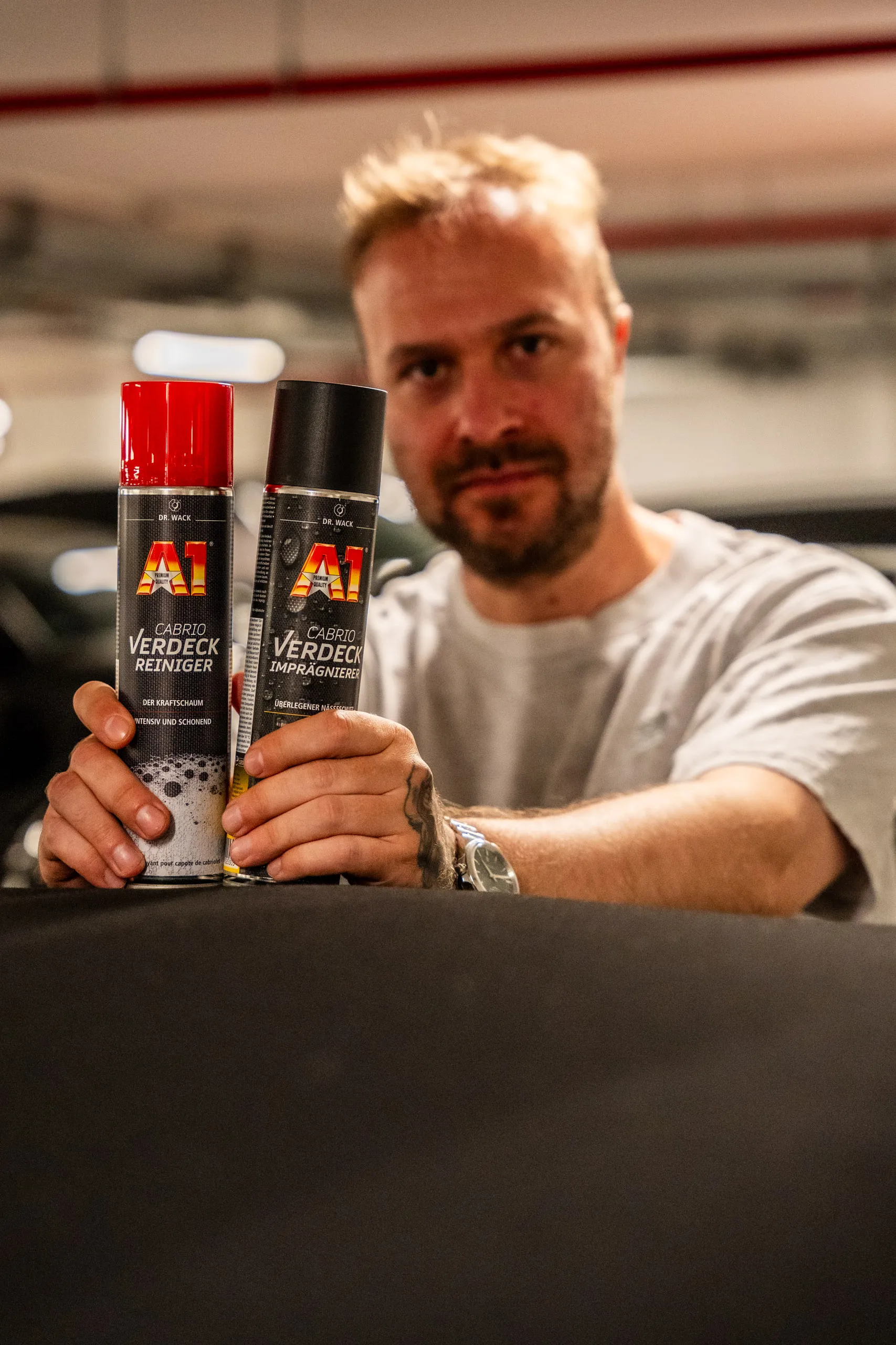 Raphael Siegmund holding two cans of A1 convertible top cleaner and waterproofer by Dr. Wack above a closed fabric roof.