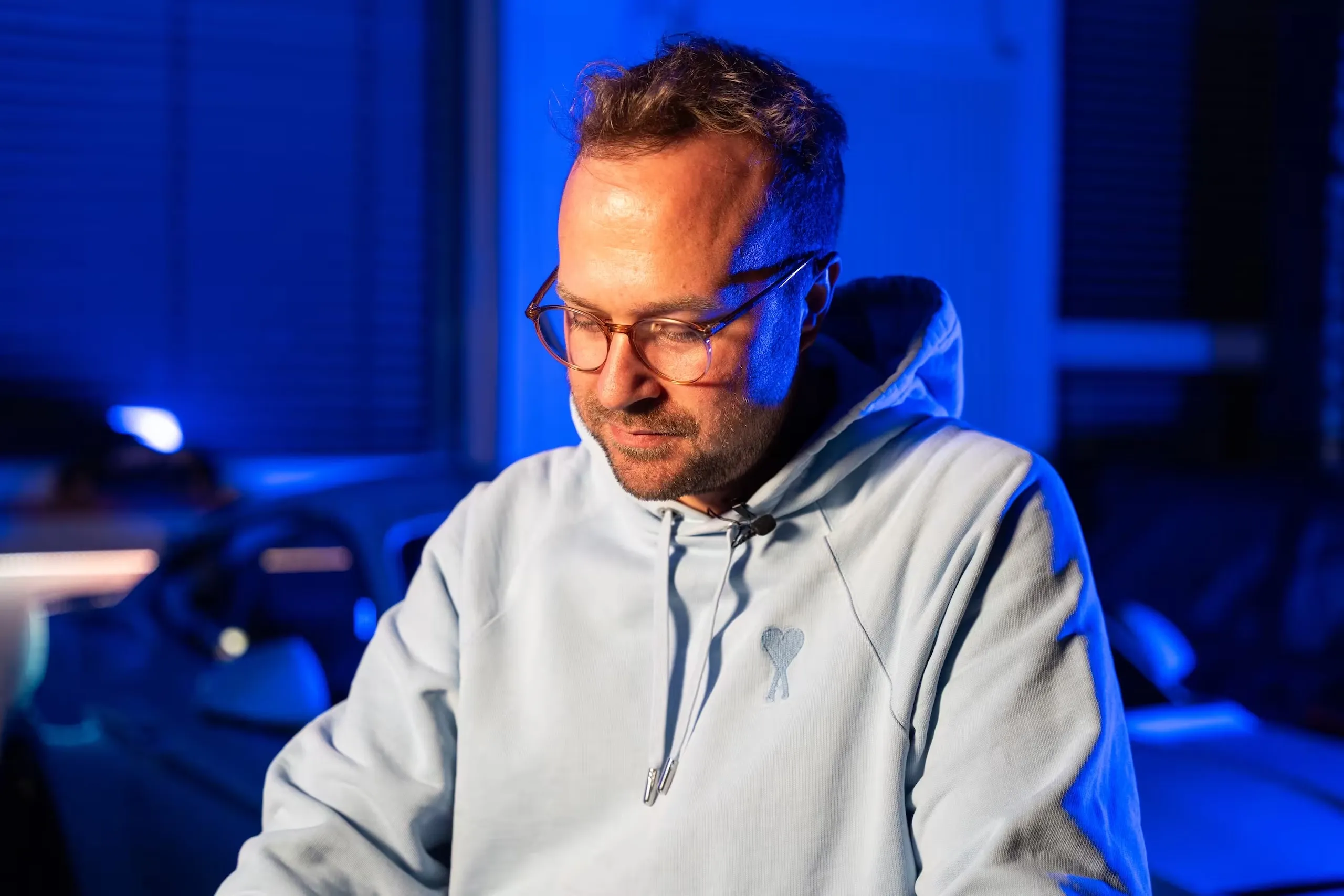 Raphael Siegmund in a light hoodie during filming, lit in blue, with a lapel microphone on his collar.