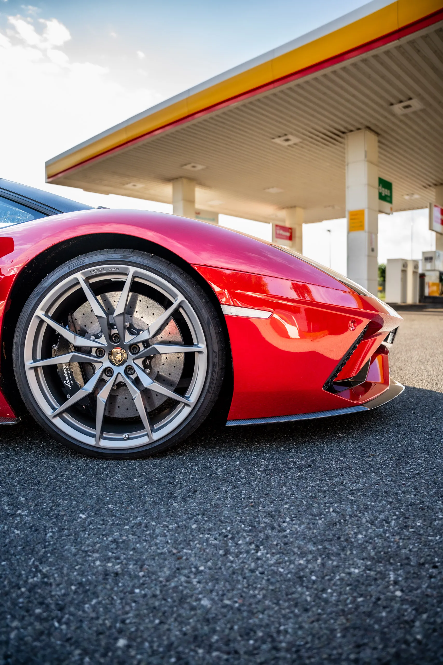 Red Lamborghini Aventador S at a petrol station, low-angle close-up of the front wheel and front splitter.