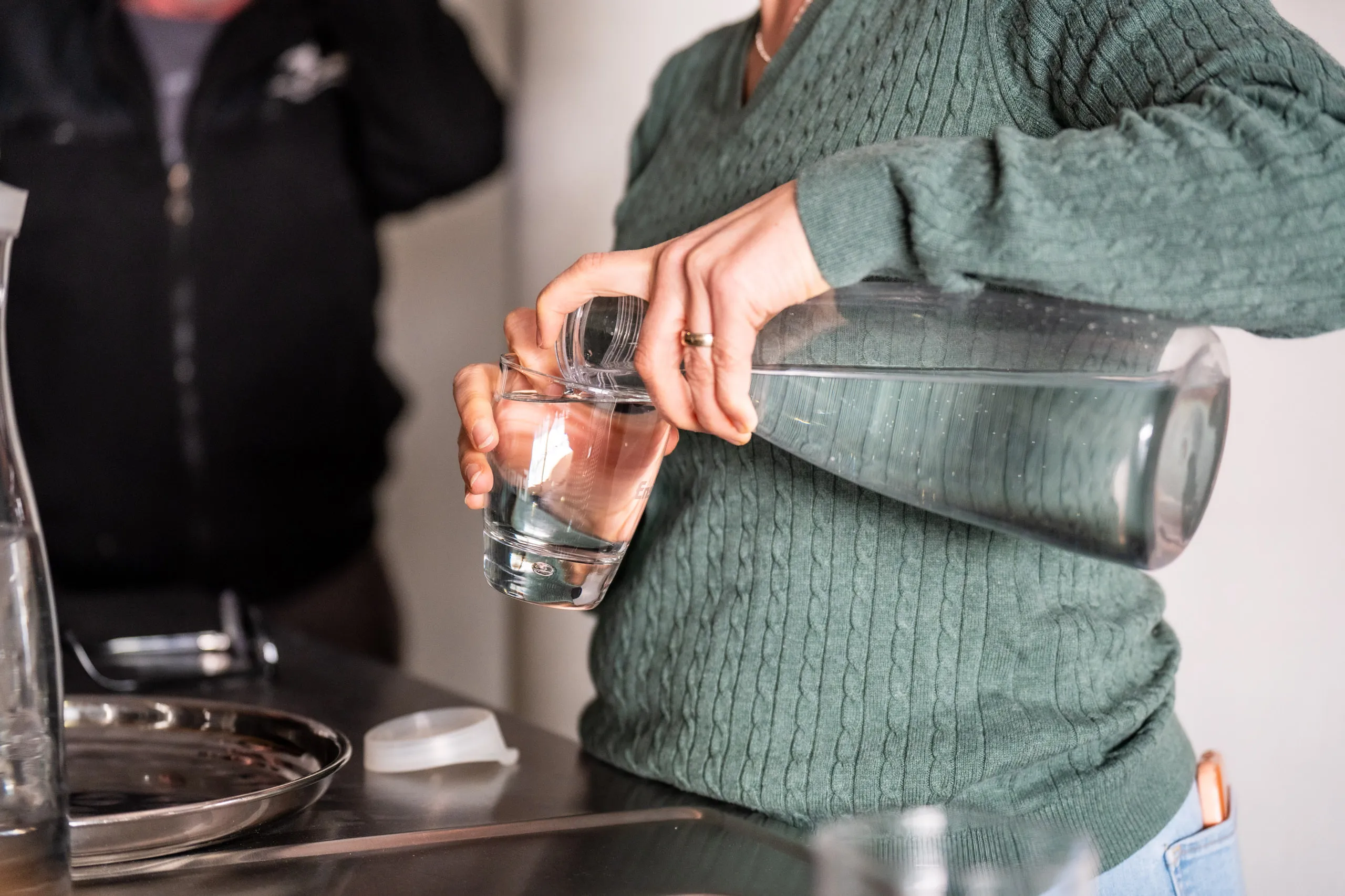 An exercise from the workshop: a participant pours water from a carafe into a glass, using a finger on the rim to feel the level.